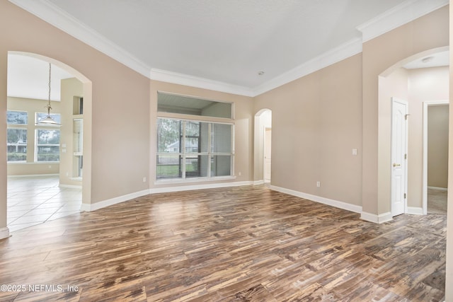 spare room featuring baseboards, arched walkways, dark wood finished floors, and ornamental molding