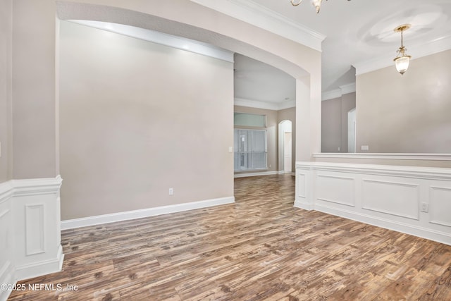 spare room featuring arched walkways, ornamental molding, wood finished floors, and baseboards