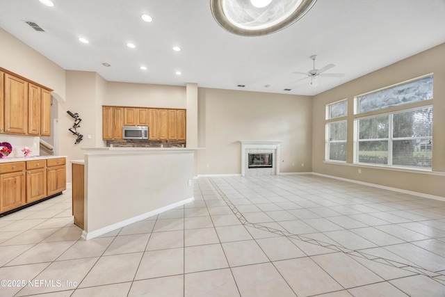 kitchen with light tile patterned floors, a tile fireplace, open floor plan, light countertops, and stainless steel microwave