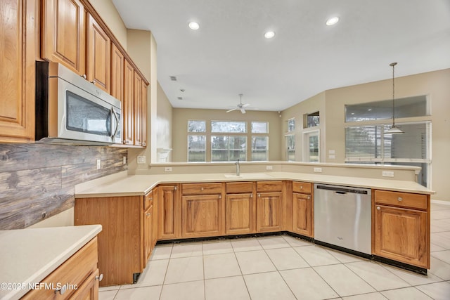 kitchen with appliances with stainless steel finishes, brown cabinets, a peninsula, light countertops, and pendant lighting