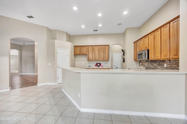 kitchen with arched walkways, light tile patterned floors, visible vents, light countertops, and stainless steel microwave