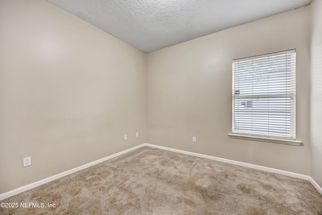 empty room with light carpet, a textured ceiling, and baseboards