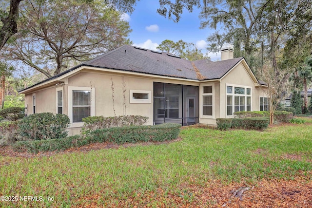 back of house featuring a chimney, stucco siding, a shingled roof, a lawn, and a sunroom