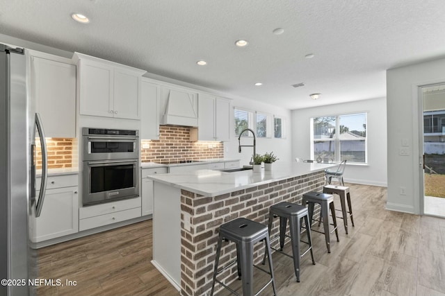 kitchen with white cabinetry, appliances with stainless steel finishes, a kitchen island with sink, and sink