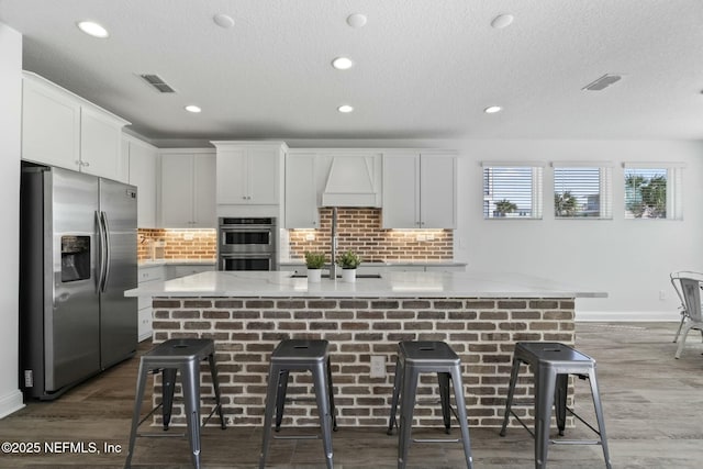 kitchen featuring a center island with sink, stainless steel appliances, white cabinets, and a kitchen bar