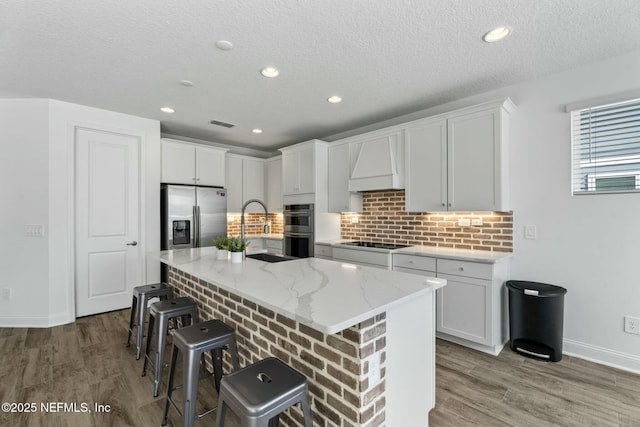 kitchen with premium range hood, appliances with stainless steel finishes, white cabinets, a kitchen breakfast bar, and a kitchen island with sink