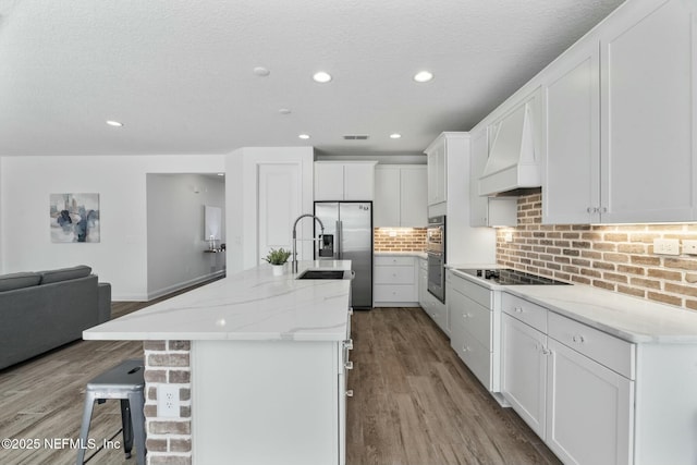 kitchen with a breakfast bar, appliances with stainless steel finishes, premium range hood, an island with sink, and white cabinets