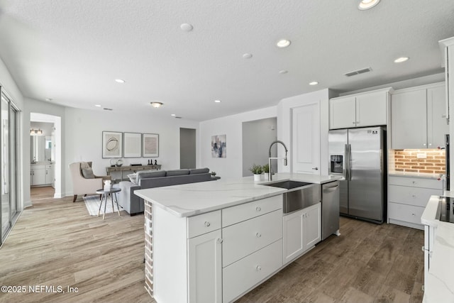 kitchen with stainless steel appliances, light stone countertops, a center island with sink, and white cabinets