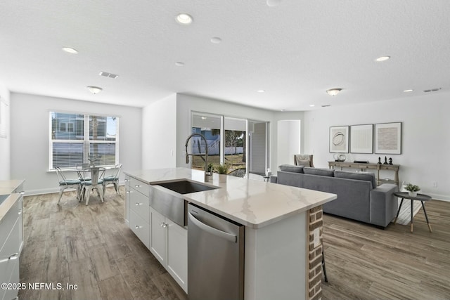 kitchen featuring sink, white cabinets, a kitchen island with sink, stainless steel dishwasher, and light stone counters