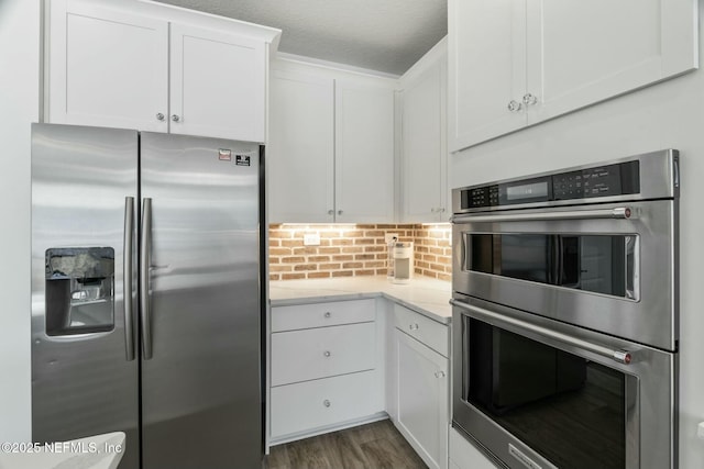 kitchen with a textured ceiling, appliances with stainless steel finishes, dark hardwood / wood-style floors, white cabinets, and backsplash