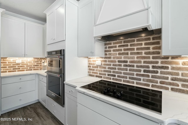 kitchen featuring white cabinetry, black electric cooktop, double oven, custom range hood, and light stone countertops