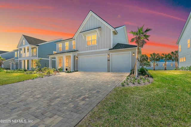 view of front facade featuring an attached garage, board and batten siding, decorative driveway, and a lawn