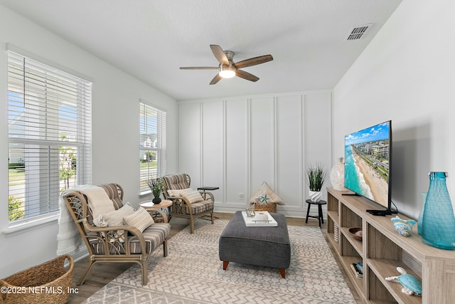 living room featuring a decorative wall, visible vents, wood finished floors, and ceiling fan