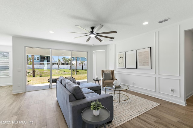 living room with light wood-style floors, visible vents, a textured ceiling, and a ceiling fan
