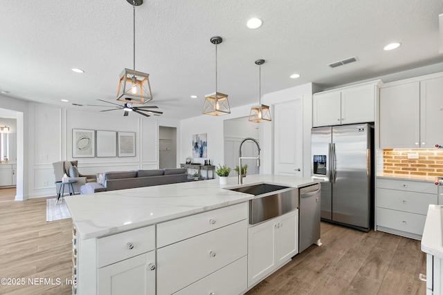kitchen with stainless steel appliances, light wood finished floors, a textured ceiling, and a sink