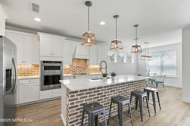 kitchen with visible vents, appliances with stainless steel finishes, light wood-type flooring, custom range hood, and decorative backsplash