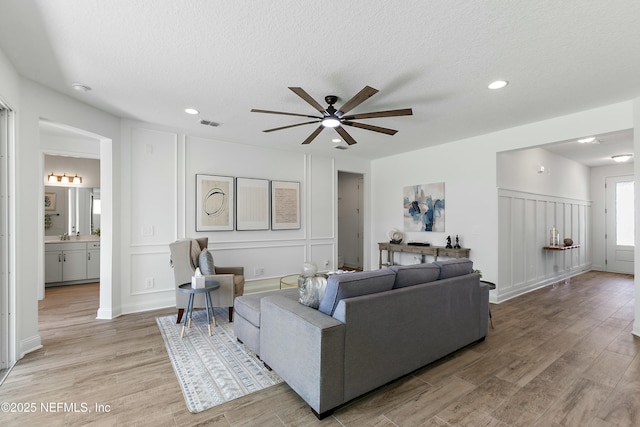 living area with a decorative wall, ceiling fan, and light wood-style flooring