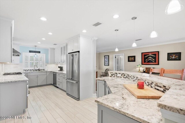 kitchen featuring appliances with stainless steel finishes, pendant lighting, decorative backsplash, crown molding, and light stone countertops