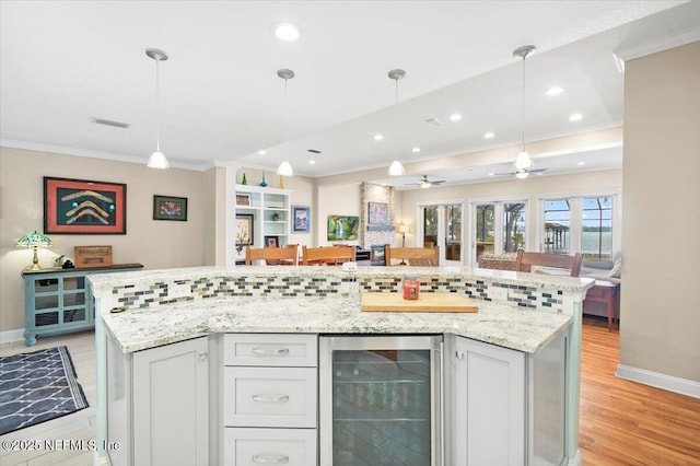 kitchen with a large island, light stone countertops, ornamental molding, and beverage cooler