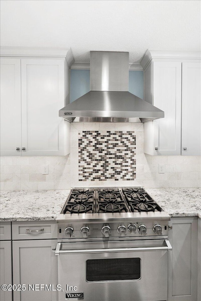 kitchen featuring tasteful backsplash, light stone countertops, wall chimney range hood, and luxury range