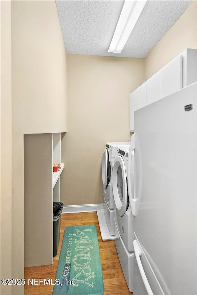 laundry room with light wood-type flooring, a textured ceiling, and independent washer and dryer