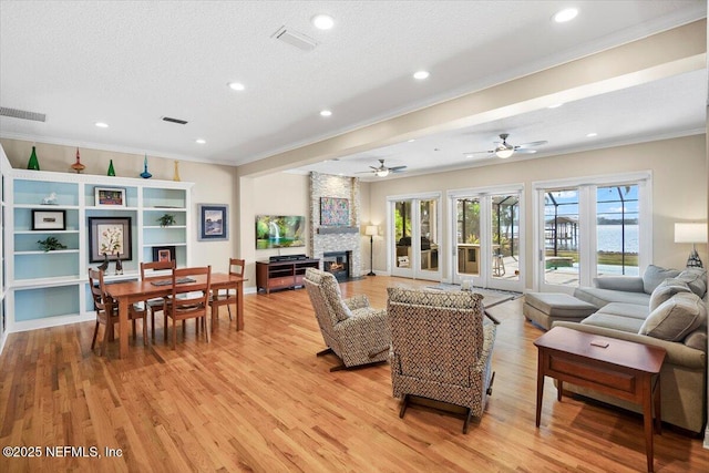 living room featuring crown molding, a stone fireplace, a textured ceiling, and light hardwood / wood-style floors