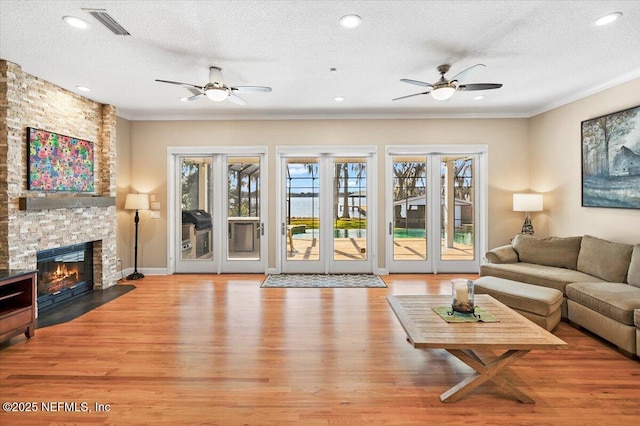 living room with a stone fireplace, ornamental molding, light hardwood / wood-style floors, and a textured ceiling