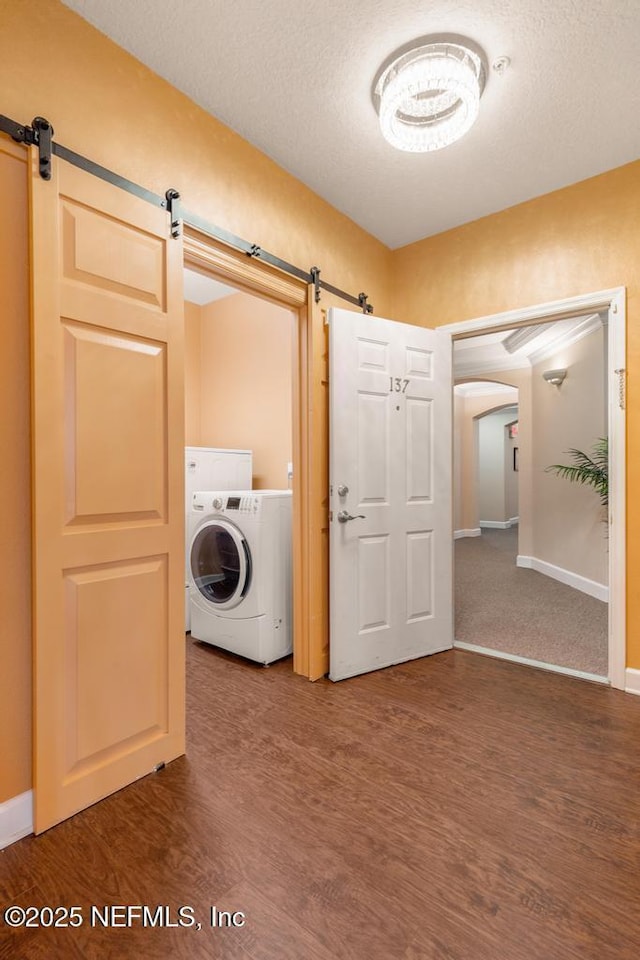 laundry room with wood-type flooring, a barn door, washer / dryer, and a textured ceiling