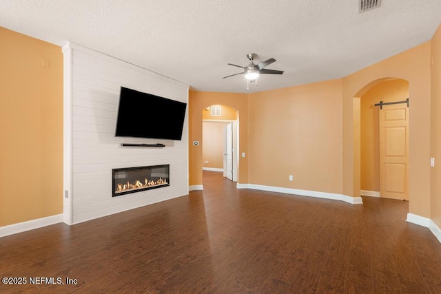 unfurnished living room with a textured ceiling, dark wood-type flooring, a barn door, and ceiling fan