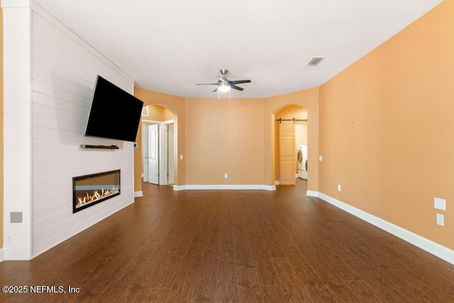 unfurnished living room featuring dark wood-type flooring, ceiling fan, a fireplace, and washer / dryer