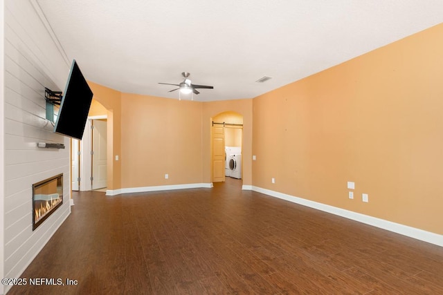 unfurnished living room featuring dark wood-type flooring, washer / clothes dryer, a large fireplace, ceiling fan, and a barn door