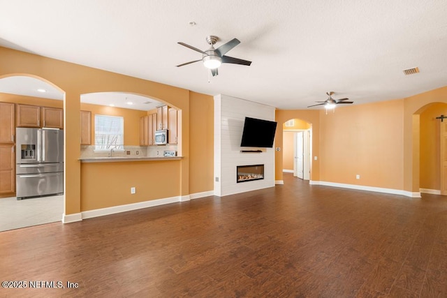 unfurnished living room with dark wood-type flooring, sink, a fireplace, and ceiling fan