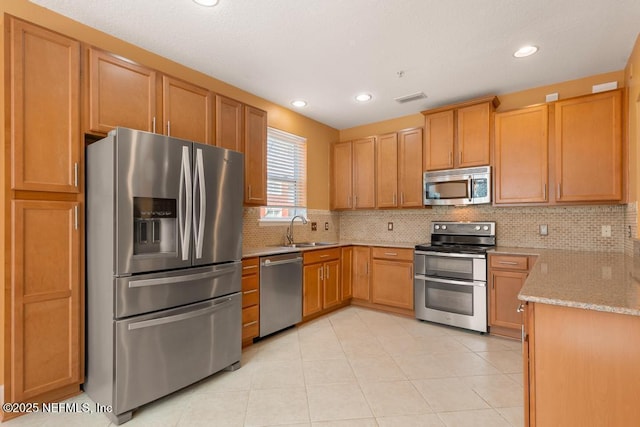 kitchen featuring light tile patterned flooring, appliances with stainless steel finishes, sink, decorative backsplash, and light stone counters