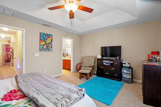 carpeted bedroom featuring ensuite bathroom, ceiling fan, and a tray ceiling