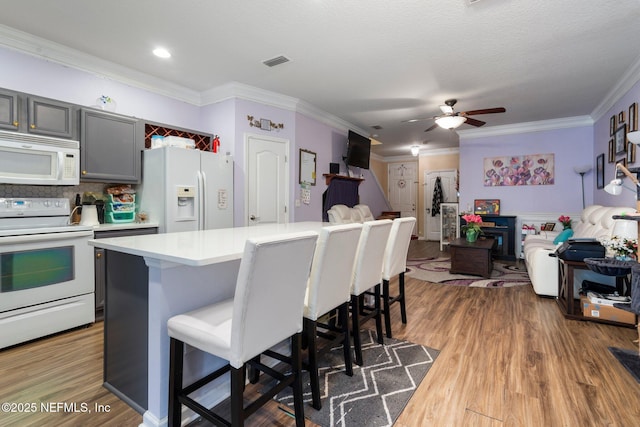 kitchen with a breakfast bar area, crown molding, gray cabinets, hardwood / wood-style flooring, and white appliances