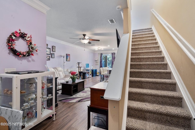 stairs with crown molding, wood-type flooring, a textured ceiling, and ceiling fan