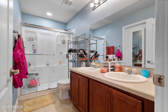 bathroom featuring toilet, a shower with shower door, a textured ceiling, vanity, and tile patterned flooring