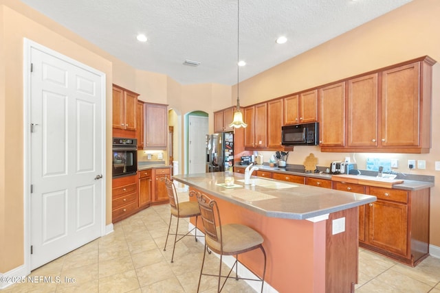 kitchen featuring sink, a breakfast bar, hanging light fixtures, black appliances, and an island with sink