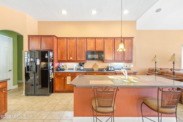 kitchen featuring pendant lighting, an island with sink, sink, a kitchen breakfast bar, and black appliances