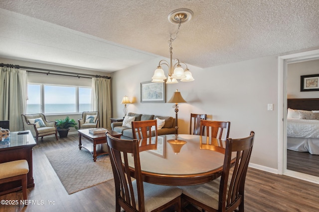 dining space featuring a water view, dark hardwood / wood-style floors, a textured ceiling, and an inviting chandelier