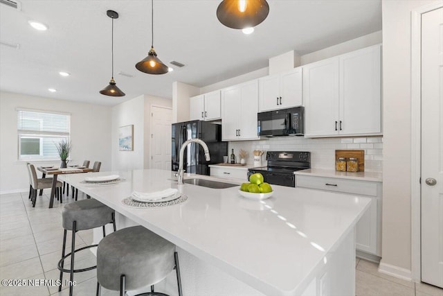 kitchen featuring decorative light fixtures, sink, white cabinets, a kitchen island with sink, and black appliances