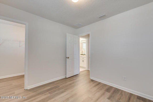 unfurnished bedroom with a closet, a walk in closet, a textured ceiling, and light hardwood / wood-style flooring