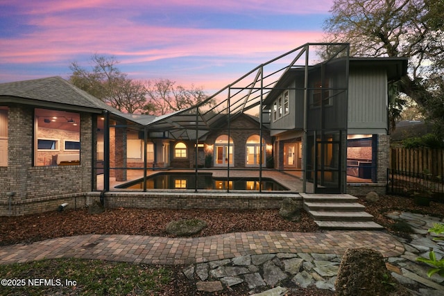 back of property at dusk with a fenced in pool, a patio area, a lanai, and fence