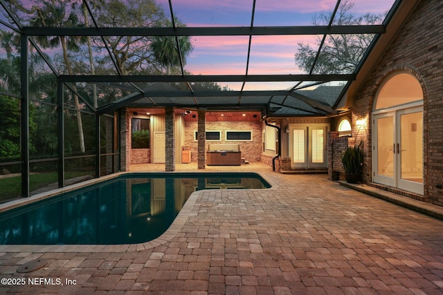 pool at dusk with a hot tub, a lanai, french doors, a patio area, and an outdoor pool