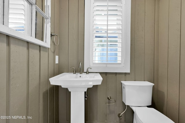 half bath featuring wooden walls, toilet, and a sink