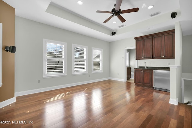 unfurnished living room with visible vents, a sink, a tray ceiling, baseboards, and dark wood-style flooring