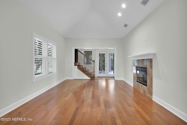 unfurnished living room with a tiled fireplace, visible vents, baseboards, and wood finished floors