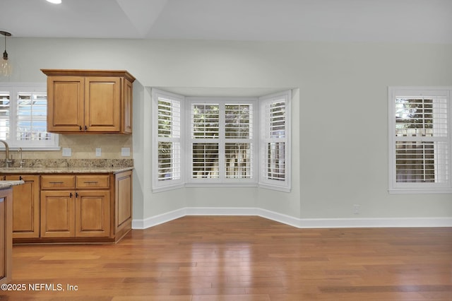 kitchen with light wood-style flooring, light stone countertops, brown cabinets, and a wealth of natural light