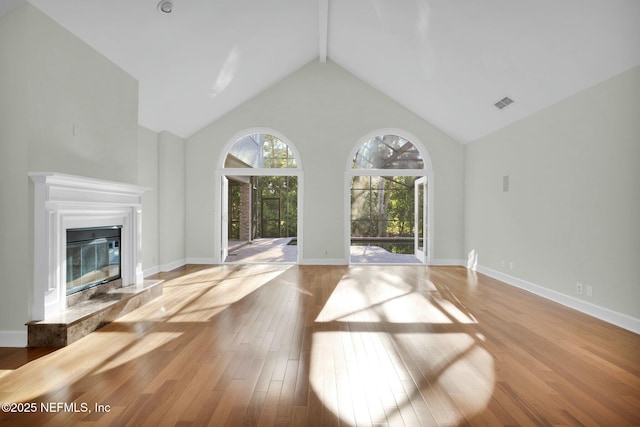 unfurnished living room featuring visible vents, beam ceiling, high vaulted ceiling, wood finished floors, and a premium fireplace