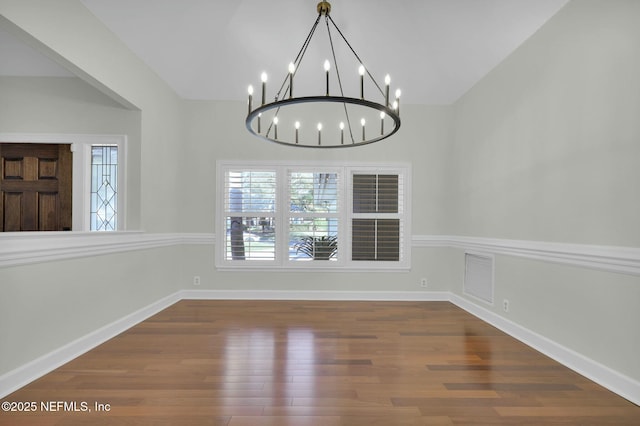 unfurnished dining area featuring wood finished floors, visible vents, baseboards, an inviting chandelier, and lofted ceiling